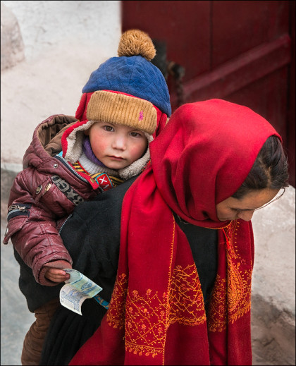 A young boy with a donation in hand is carried on his mother's back up to the monastery.