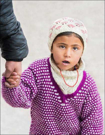 A young girl holds on to her father's hand tightly as they navigate the crowds.