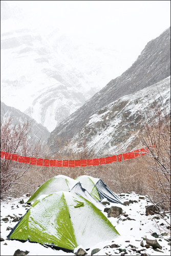 Tents in the snow under a string of Buddhist prayer flags.